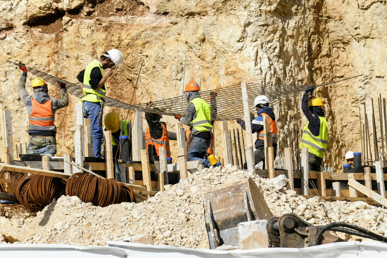 A crew of construction workers in hard hats and high-visibility vests installing rebar at an active excavation site.